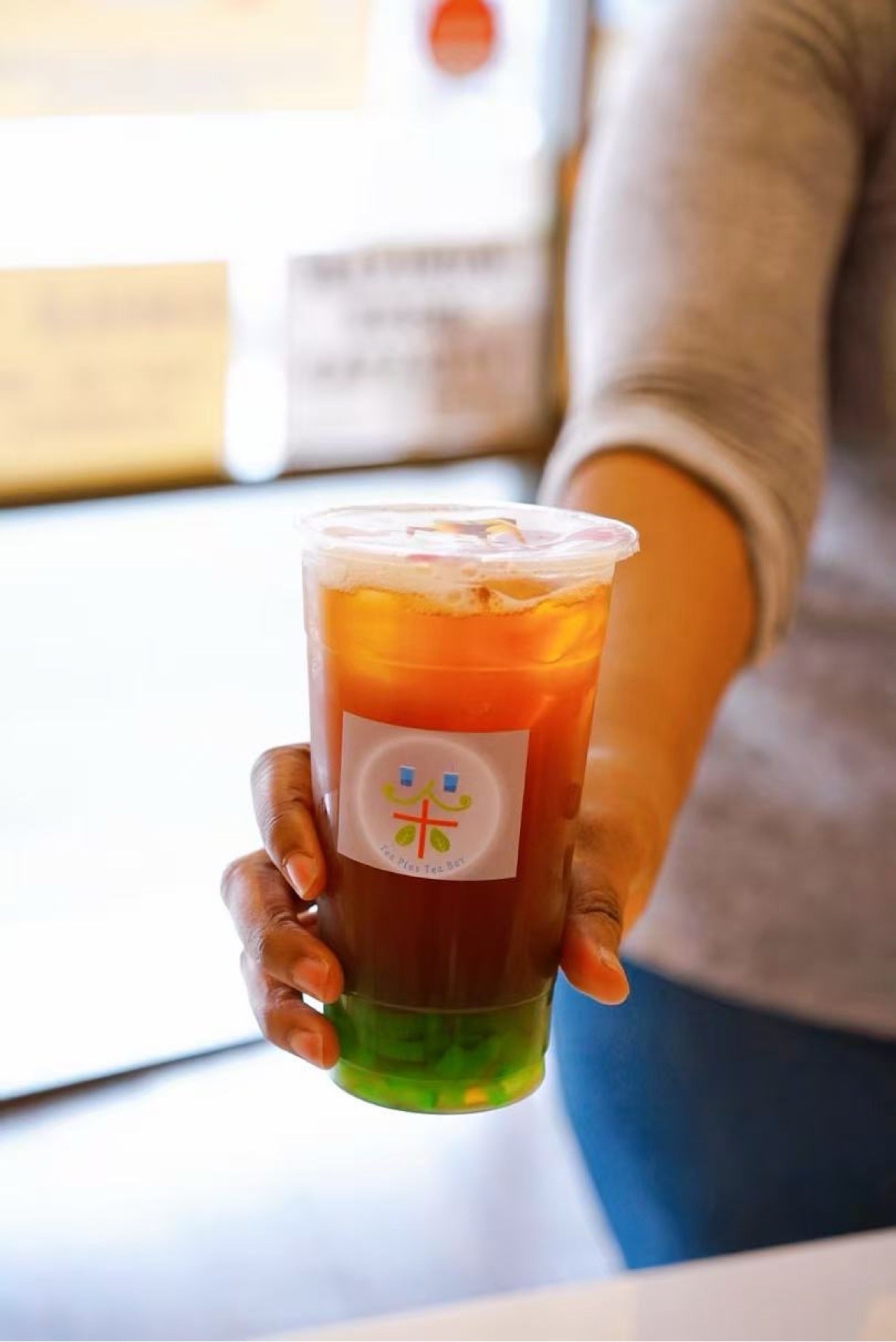 A freshly brewed iced tea in a Tea Plus Tea Bar cup, handed over the counter